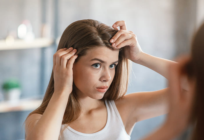分け目の薄毛を気にしながら鏡を見る女性のイメージ写真
